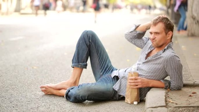 醉汉躺在外面的人行道上。男子从纸袋里喝啤酒