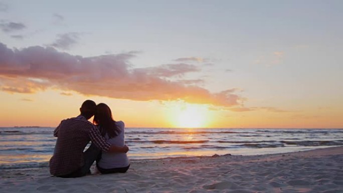 一对年轻夫妇在海上欣赏日落。坐在沙滩上的怀抱中