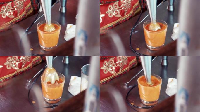 酒保在酒吧用搅拌机在玻璃中混合橙色物质。制作鸡尾酒