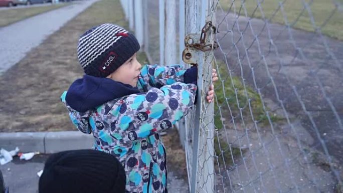 男孩试图打开高高的栅栏上的锁