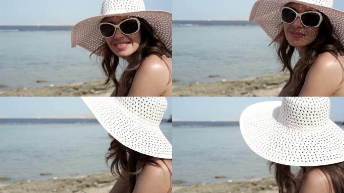 戴着帽子和太阳镜的美女在海滩上晒日光浴
