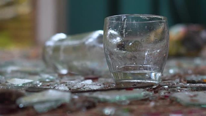 碎玻璃背景上的一杯伏特加。掉落的瓶子