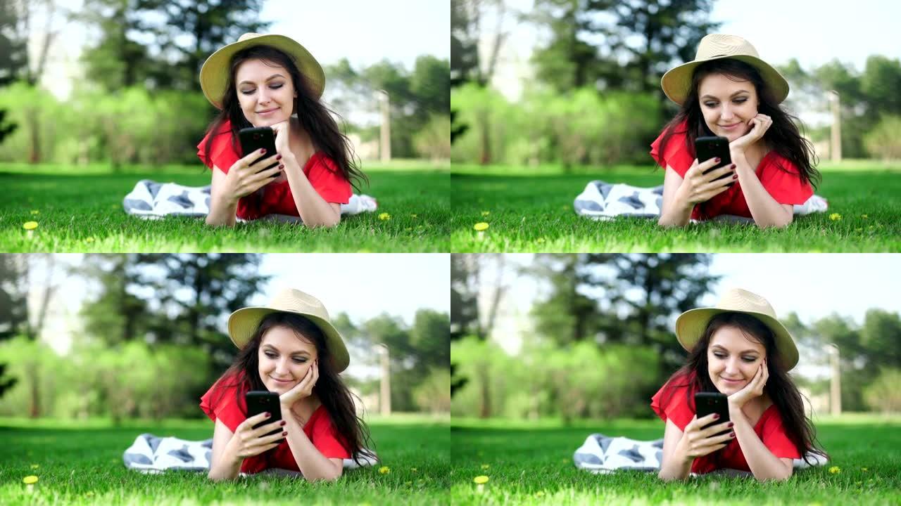 年轻女子用手机空红屏躺在绿草地上。