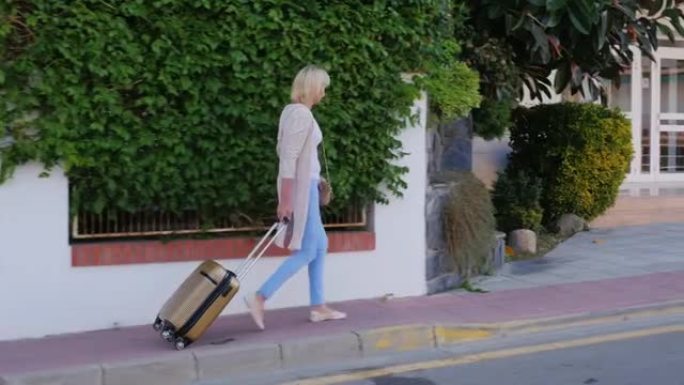 带着轮子上的旅行袋的女人来到酒店门口。抵达酒店或度假