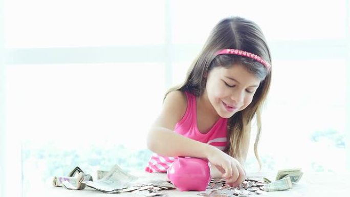 快乐的小女孩把硬币放进她的粉色存钱罐。