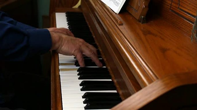 年长的男性手从侧面弹奏立式钢琴
