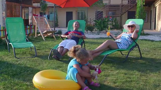 带饮料的家庭在小度假酒店草地上的日光浴躺椅上放松