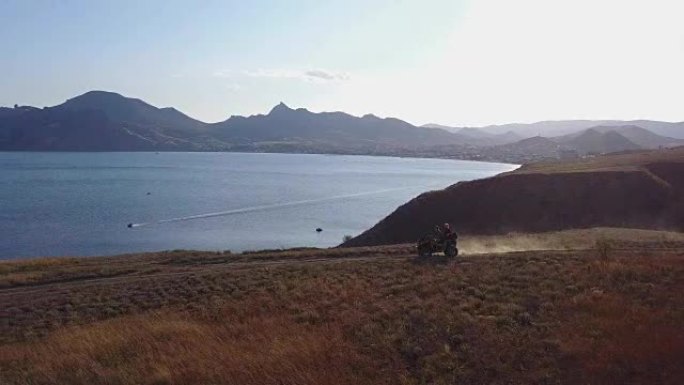 一对年轻游客的无人机在乘坐ATV运输工具时，正在缓慢地在日落时欣赏美丽的海景。夫妇正在海边的山上骑四