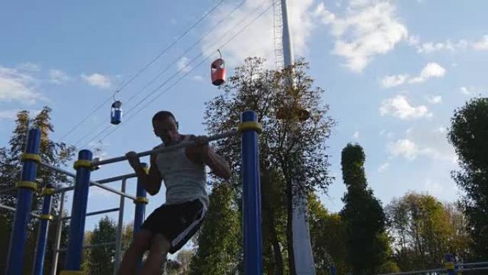 强壮的肌肉男人在公园里做肌肉锻炼。年轻运动员在室外单杠上做俯卧撑。健身肌肉男夏天在外面训练。运动员停