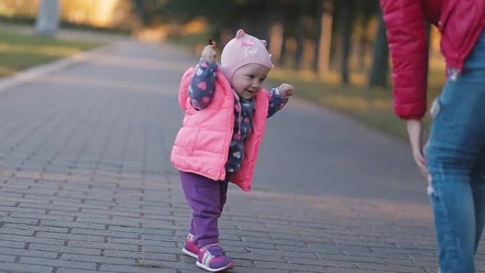 在秋天的公园小女孩迈出第一步，她的母亲帮助她。