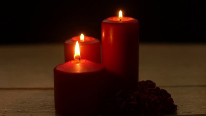 在浪漫的时光里，三根红蜡烛在木桌上燃烧和玫瑰