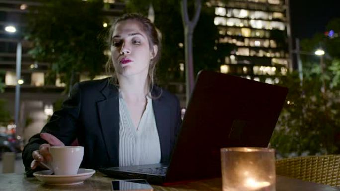 年轻的女商人晚上坐在咖啡馆里，在笔记本电脑上工作