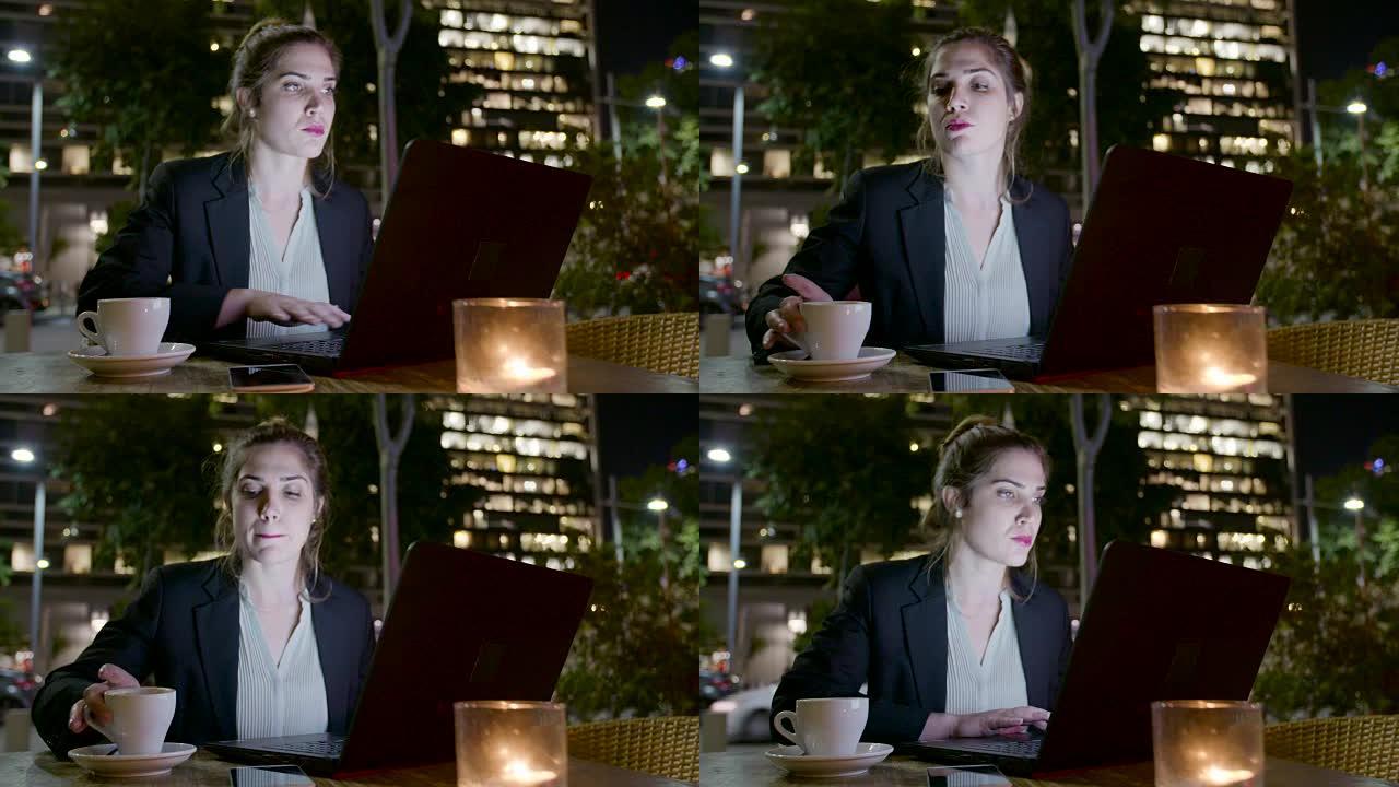 年轻的女商人晚上坐在咖啡馆里，在笔记本电脑上工作
