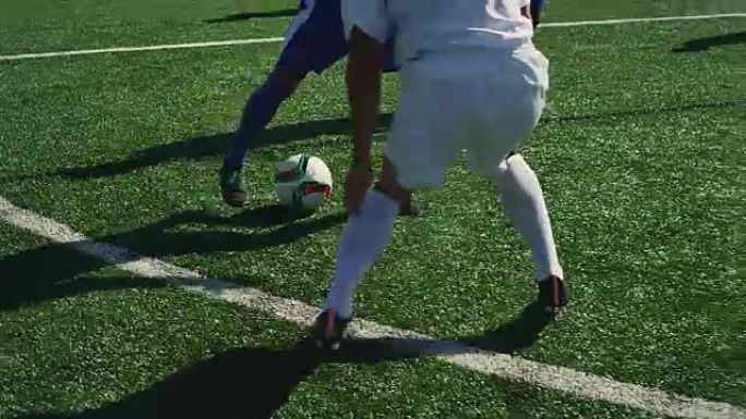 一名足球运动员在球场上运球，对手为他严密辩护。