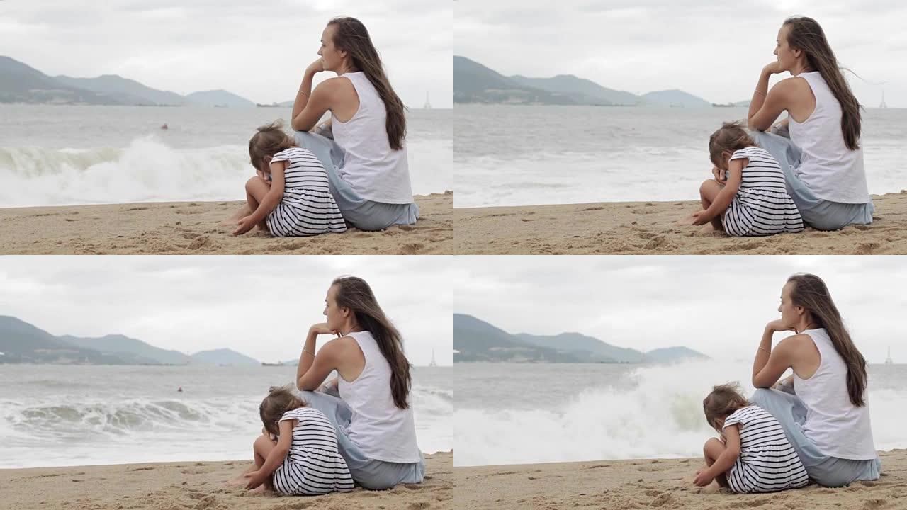 母亲带着一个女儿坐在沙滩上，背对着镜头。