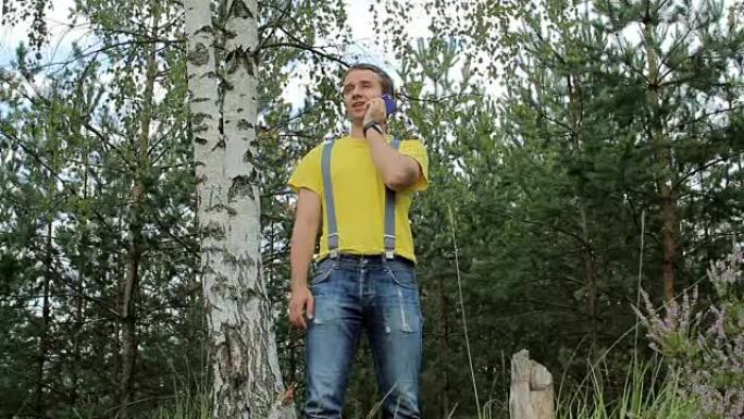 徒步旅行者穿过森林，在电话里聊天。黄色t恤和带吊带的牛仔裤。野外技术