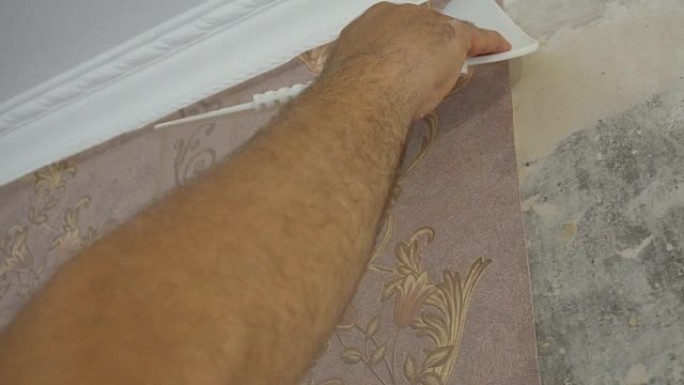 将墙纸粘贴在墙上的过程，工人的手用刮刀夹紧使墙纸光滑