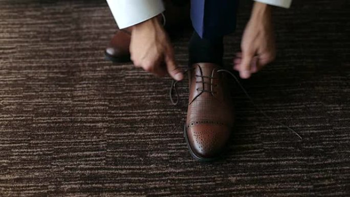 男人在棕色皮鞋上系鞋带。