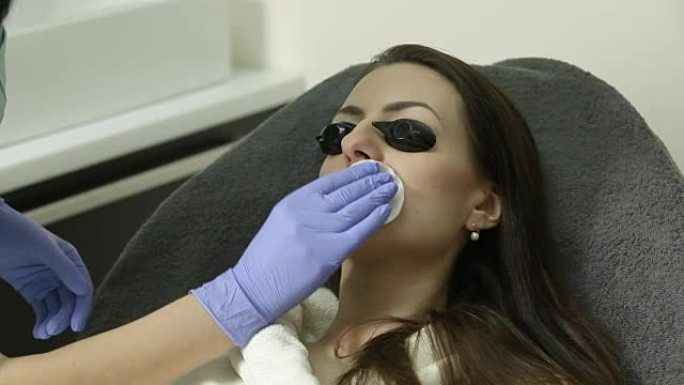 手术前，美容师用棉质海绵擦拭女性患者的面部。消毒