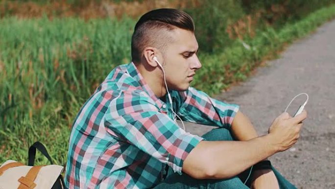 坐在马路上的男孩戴着耳机听音乐。等。汽车。搭便车