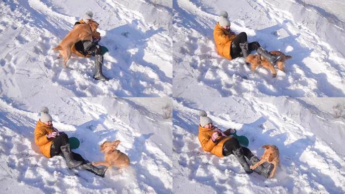 一个女孩在冬天的雪公园里和狗玩得很开心，十几岁的女孩和狗躺在雪地里，阳光明媚的寒冷日子。