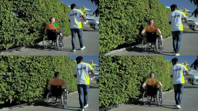 一个愉快的志愿者帮助一个轮椅主持人的后视图