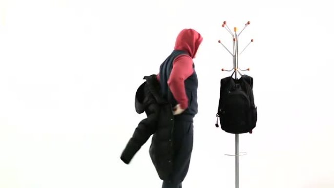 一个年轻人脱下背包，把冬天的夹克挂在衣架上。