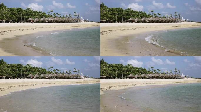 温暖的海浪在热带度假胜地的沙滩上奔跑，带有雨伞和躺椅
