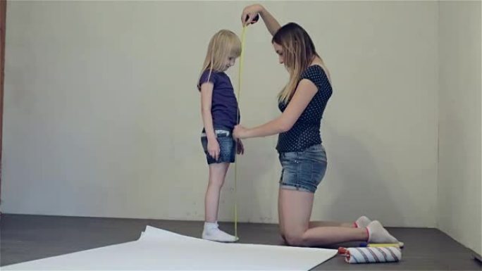 在公寓维修期间，母亲正在用胶带或轮盘赌测量女儿的身高。