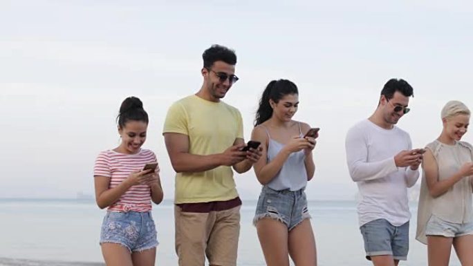 使用手机在海滩上行走的人们微笑，年轻游客在线组网