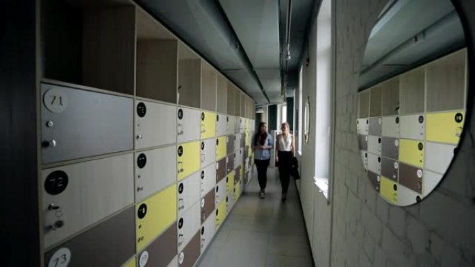 两名妇女正走在办公室走廊上，穿着衣服的盒子