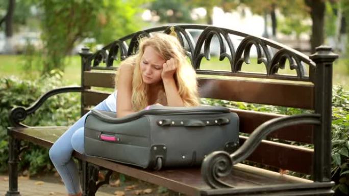 悲伤的女孩拿着手提箱坐在长凳上。
