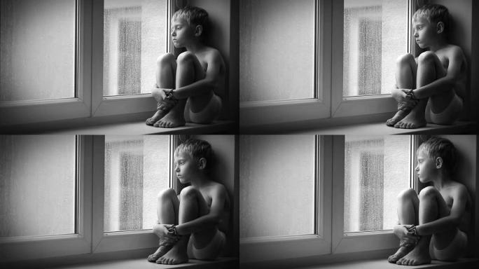 孤独的小男孩透过窗户玻璃看着雨滴，坐在窗台上