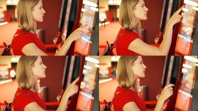 穿着红色t恤的年轻美女在电影院的自动售货机上购买电影票