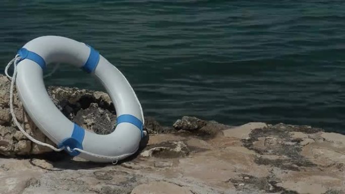 一个白色的救援浮标靠在靠近水的一块石头上，镜头正在延时。