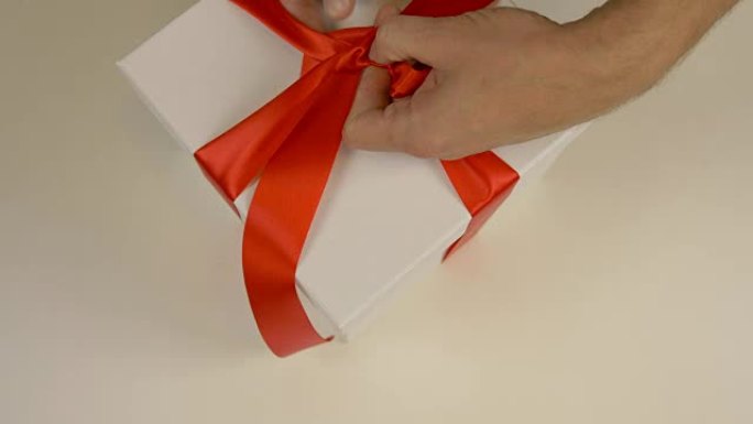 快速运动。包装白色礼品盒。高加索人手包装礼品盒。男人的手在白色纸板箱上系上红丝带。俯视图特写。红色缎