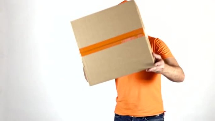 穿着橙色制服的送货员向相机扔了一个大包裹。浅灰色背景，慢动作工作室拍摄