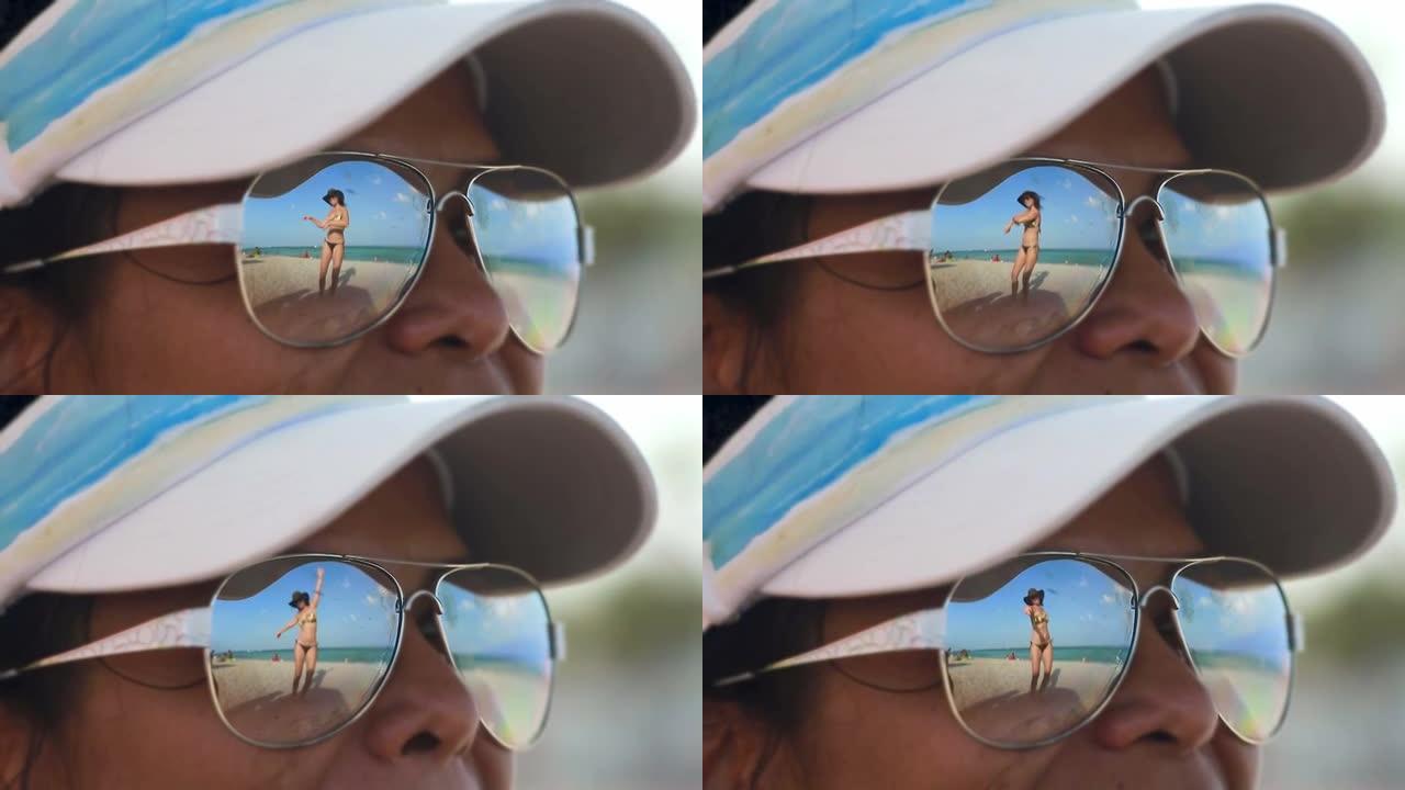 女人看着另一个戴着墨镜在海滩上跳舞的女人