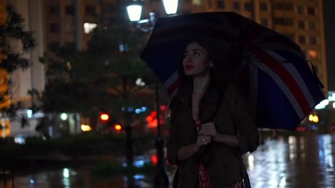 女孩带着英国国旗伞在雨夜散步，慢动作视频