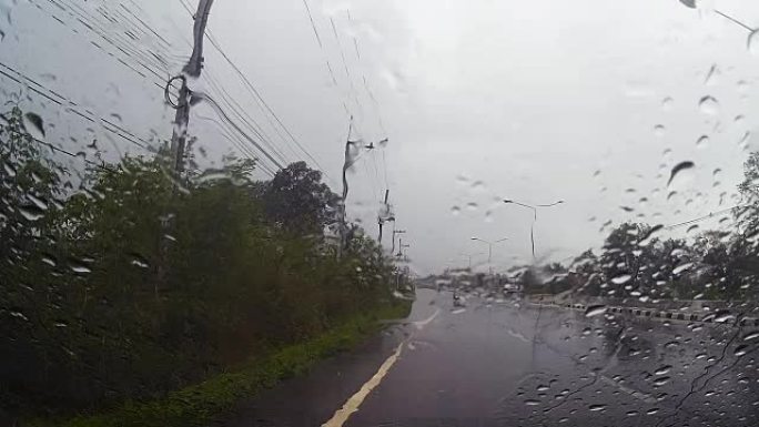 通过带有雨滴的汽车挡风玻璃的道路视图，在雨中行驶。