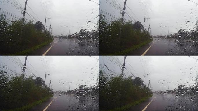 通过带有雨滴的汽车挡风玻璃的道路视图，在雨中行驶。