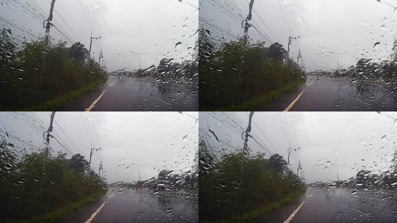 通过带有雨滴的汽车挡风玻璃的道路视图，在雨中行驶。