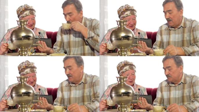 老年夫妇从老式的俄罗斯茶壶茶壶喝茶，然后在平板电脑上观看照片。一个留着小胡子的男人和一个女人在讨论这