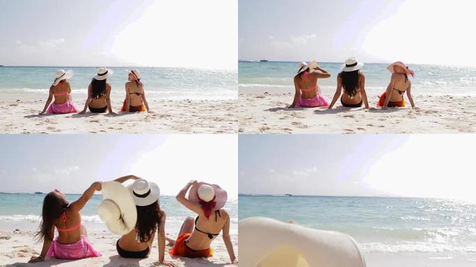 穿着比基尼在海滩上的三个女孩的后视图，享受晒晒话，女人在暑假脱下草帽游客