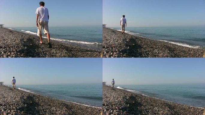 男子从相机沿着岩石海岸行走