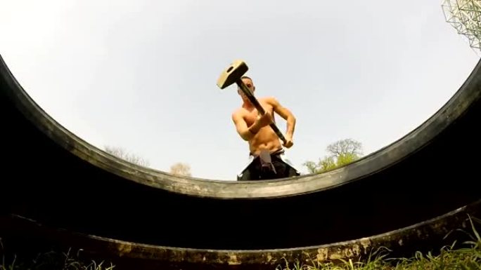 一个肌肉男用锤子敲打轮胎的特写