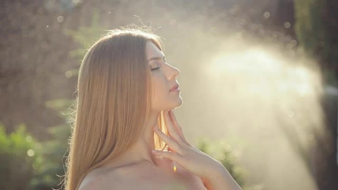 性感的金发女郎摆姿势在花园里的比基尼在夕阳下的水花
