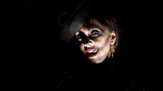 万圣节派对，夜晚，暮色中令人恐惧的女人肖像，在光线中。穿着黑色女巫服装化妆得很糟糕的女人