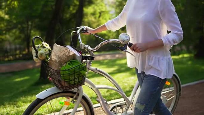 女人的手握着城市自行车的车把的特写视图，篮子里放着鲜花和书。在城市公园享受时光的女人。夏季