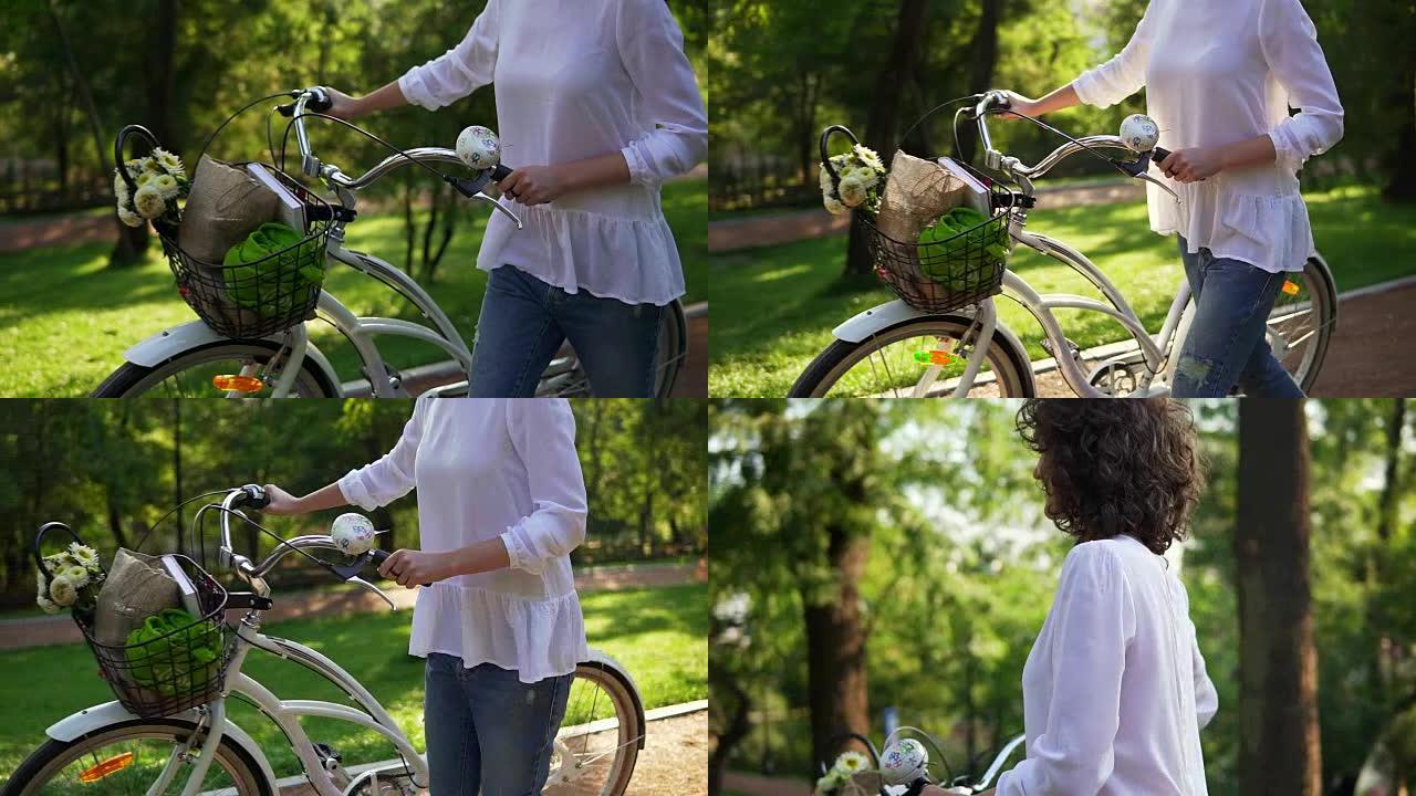 女人的手握着城市自行车的车把的特写视图，篮子里放着鲜花和书。在城市公园享受时光的女人。夏季